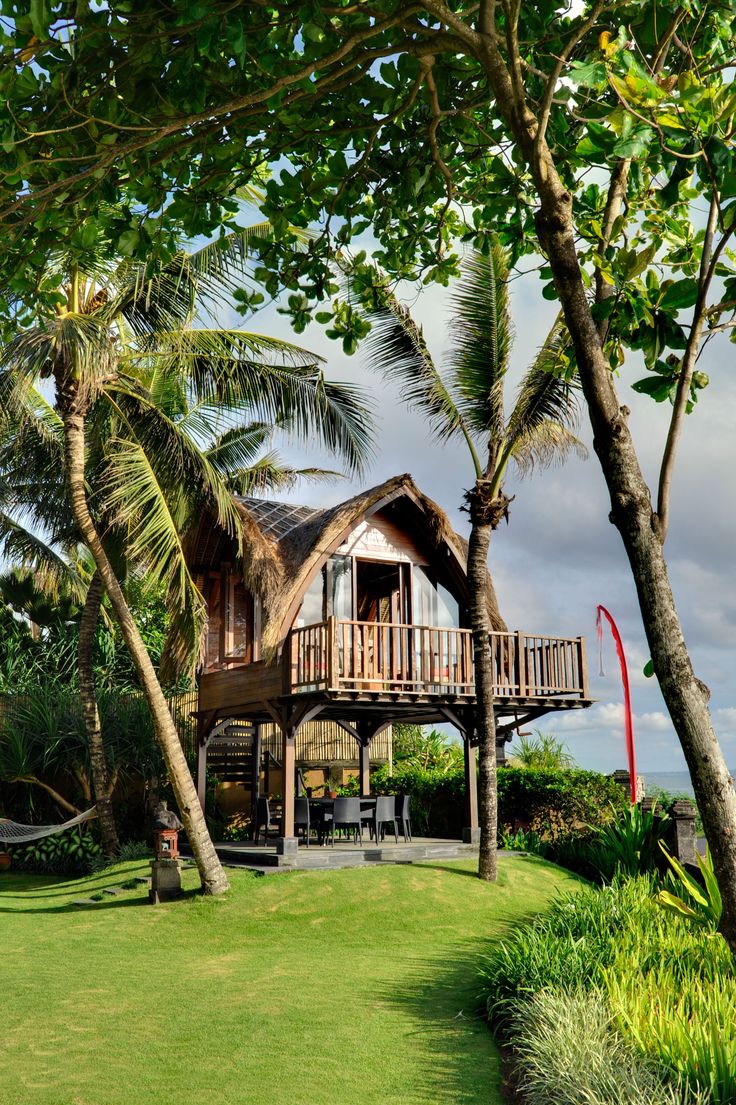 a wooden house sitting on top of a lush green field next to trees and palm trees