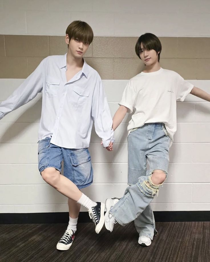 two young men standing next to each other in front of a white wall holding hands