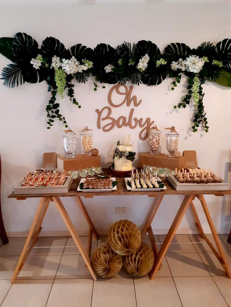 a baby shower is set up on a table with desserts and greenery around it