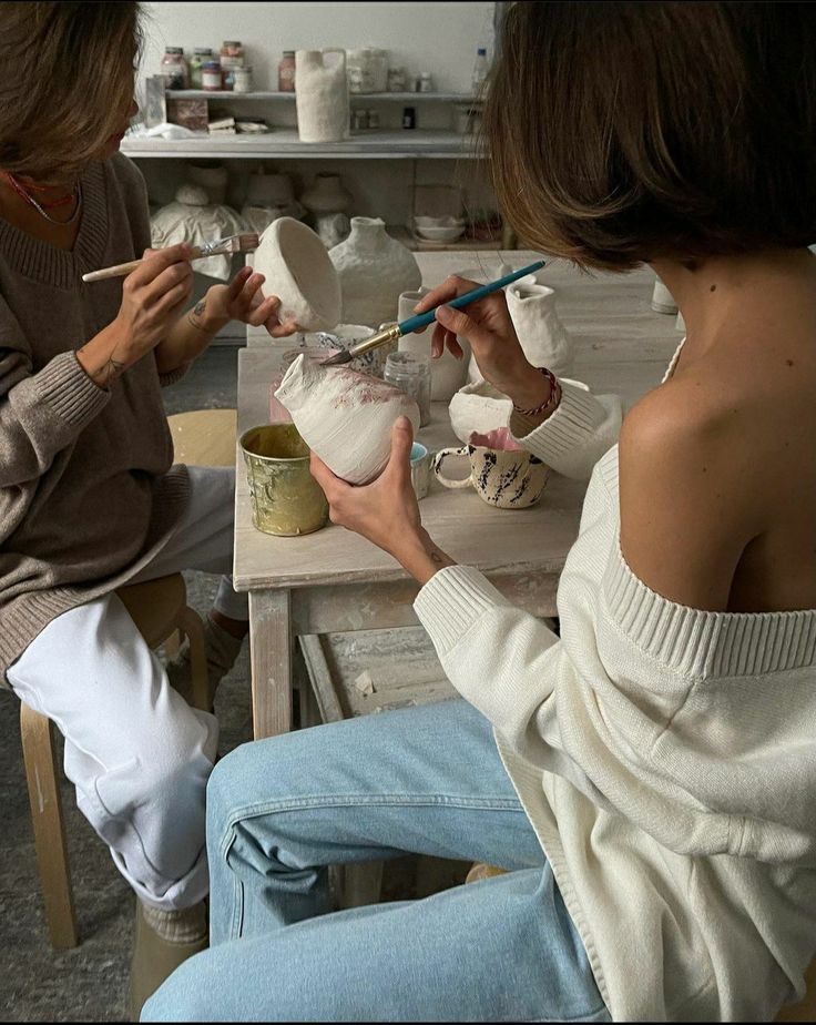 two women sitting at a table with bowls and paintbrushes in their hands,