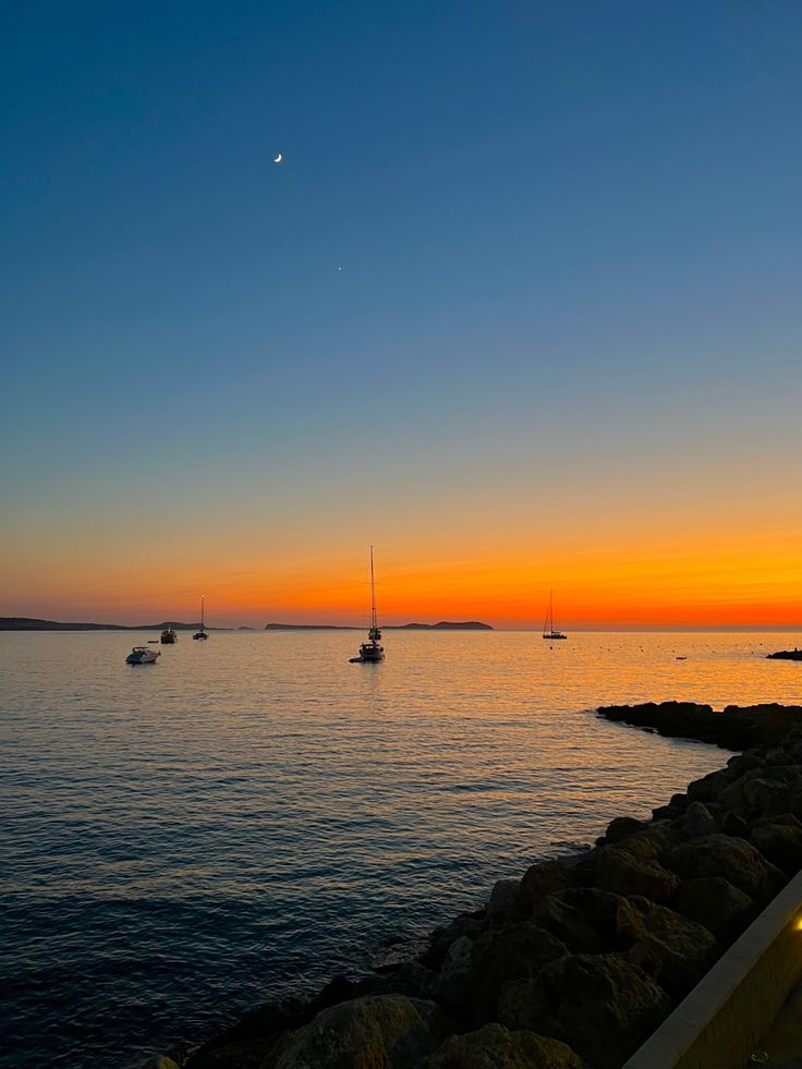 the sun is setting over the water and boats are in the distance