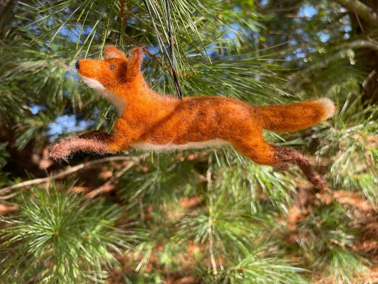 a needle felt fox ornament hanging from a pine tree