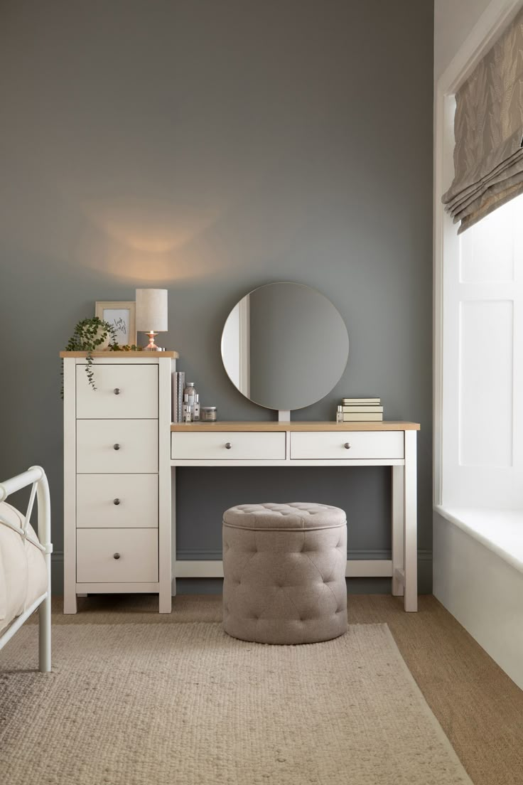 a bedroom with gray walls, white furniture and a large round mirror on the wall