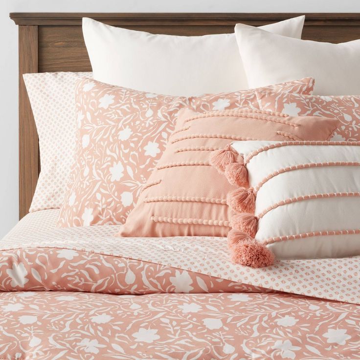 a bed with pink and white pillows on top of it, along with a wooden headboard