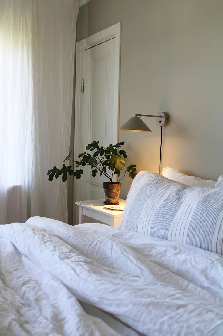 a bed with white linens and a potted plant