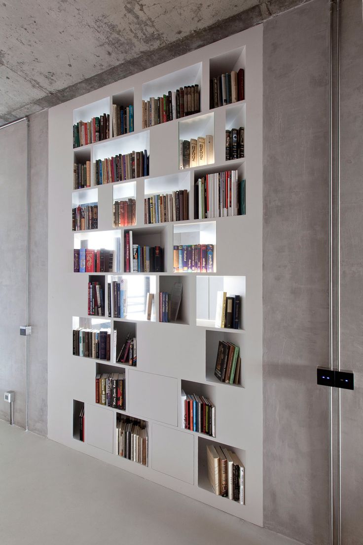 a white book shelf filled with lots of books next to a wall mounted refrigerator freezer