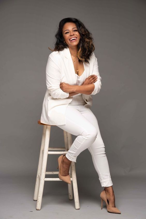 a woman sitting on top of a stool with her arms crossed and smiling at the camera