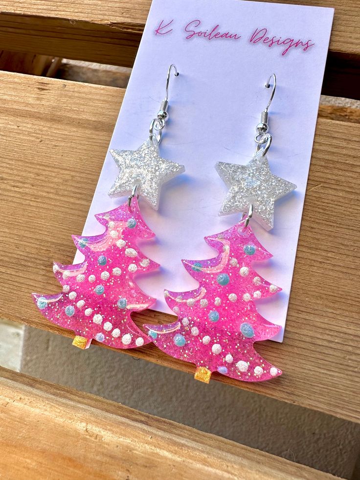 pink and silver christmas tree earrings with glitter stars on the top, sitting next to a card