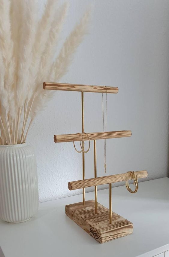 a white vase sitting on top of a table next to a wooden stand with a plant in it