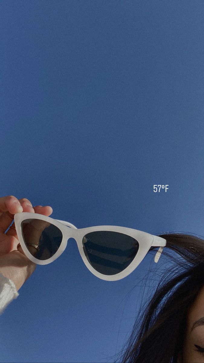 a woman holding up her sunglasses in front of the blue sky with an arrow on it