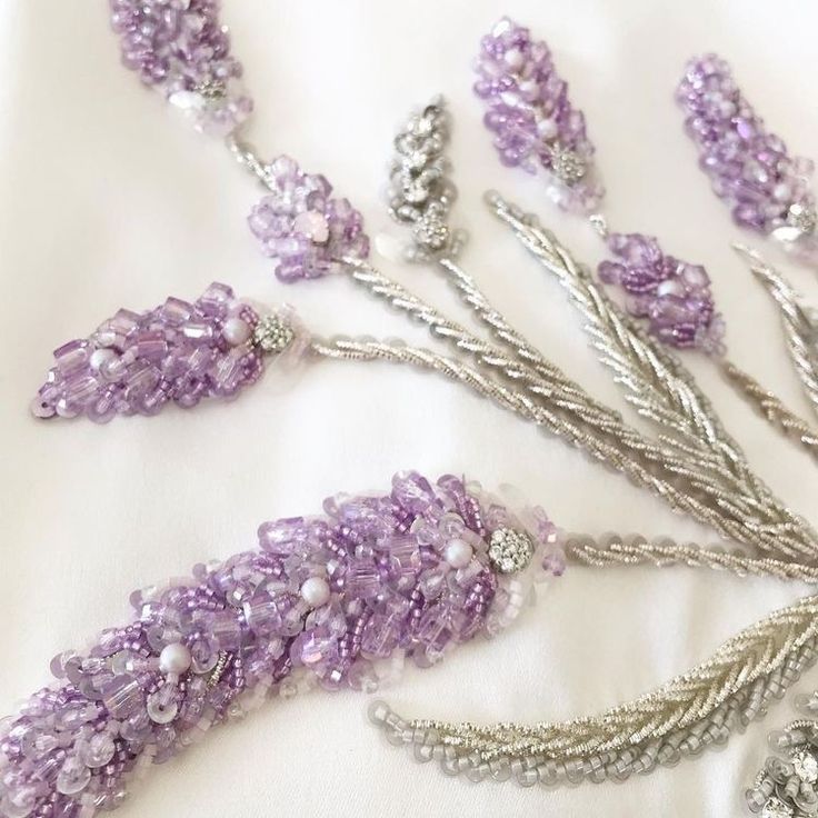 some beads and chains are laying on a white sheet with purple flowers in the middle