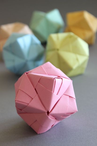 four different colored origami balls sitting next to each other on a gray surface