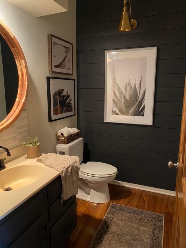 a bathroom with wood flooring and black walls, including a round mirror above the toilet