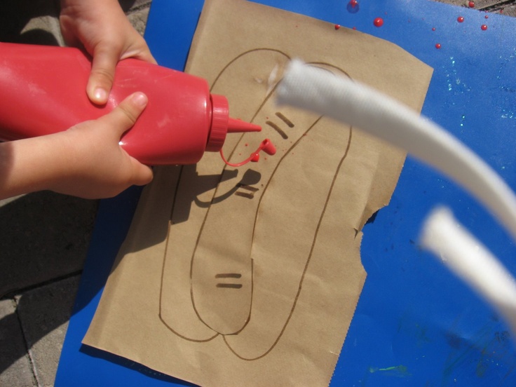 a child is using a red spray bottle to paint the face of a man on a piece of cardboard