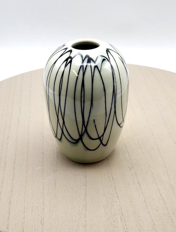 a white and black vase sitting on top of a wooden table