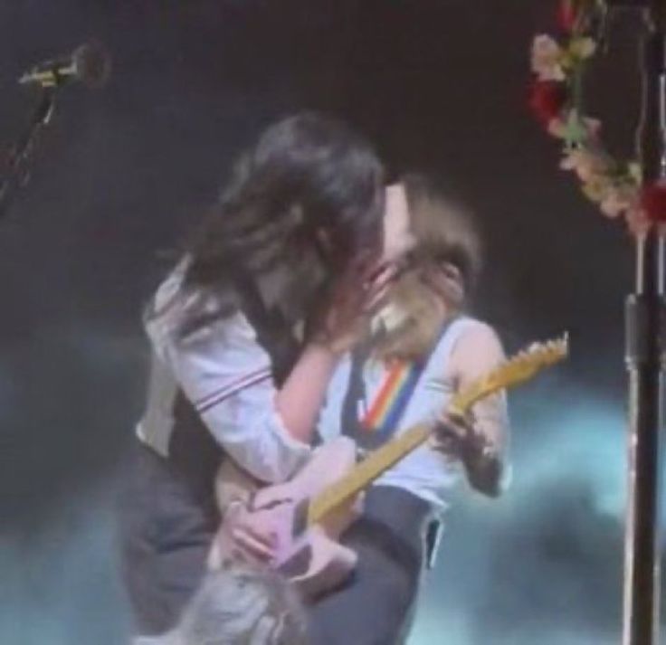 a man and woman kissing on stage with guitars