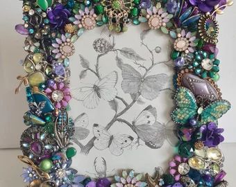 a photo frame with flowers and butterflies on the front, surrounded by other jeweled objects