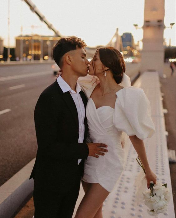 a man and woman are kissing on the side of a road while wearing white dresses