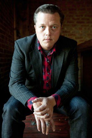 a man sitting on top of a wooden bench wearing a suit and red checkered shirt