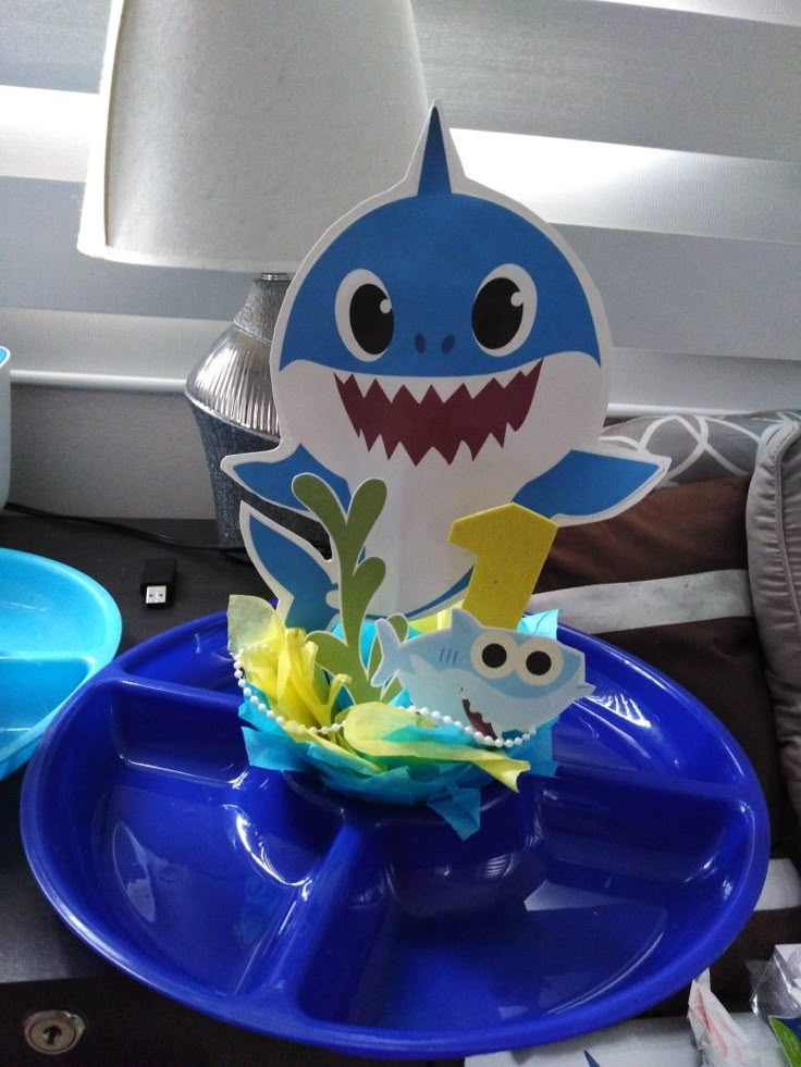 a blue plate topped with a shark cutout next to a lamp on a table