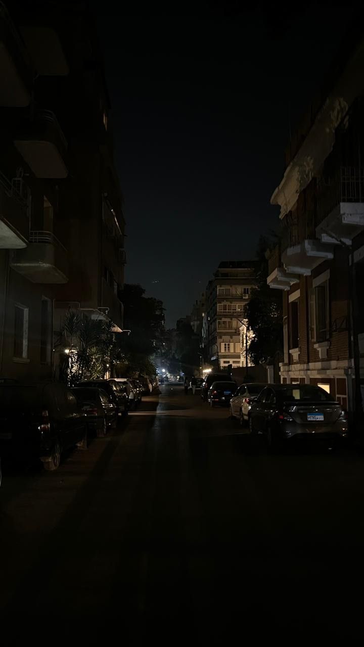 an empty street at night with cars parked on the side and buildings in the background