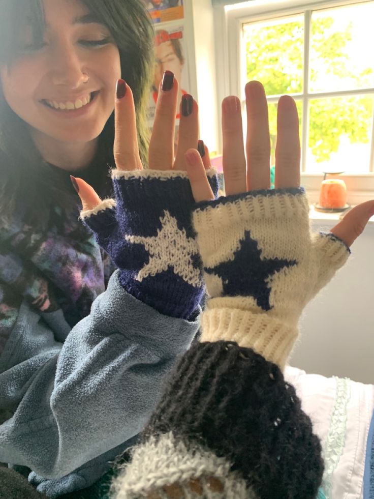 a woman is showing off her hand knitted mitts with stars on the fingers