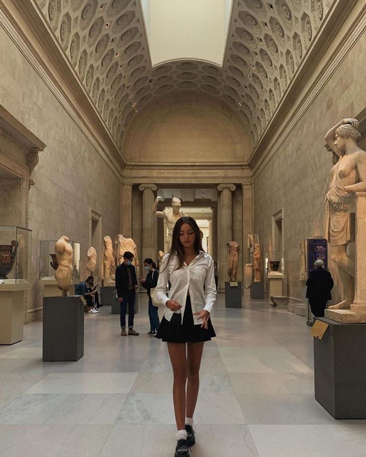 a woman is standing in an art museum looking at the camera and posing for a photo