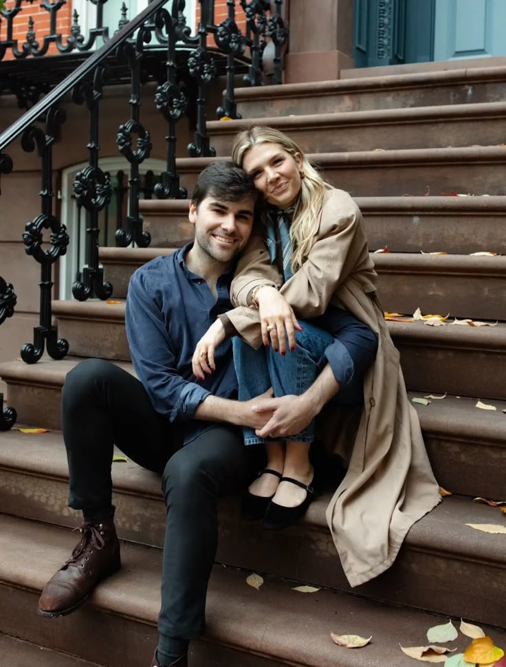 a man and woman are sitting on the steps in front of some stairs with their arms around each other