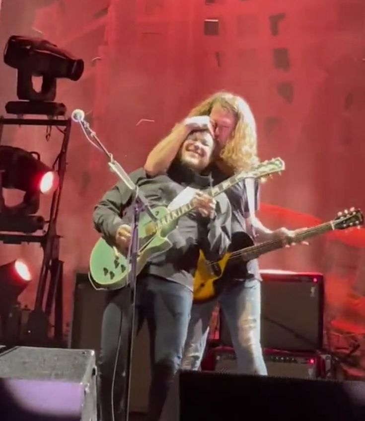 two men standing on stage with guitars in their hands and one man holding his head