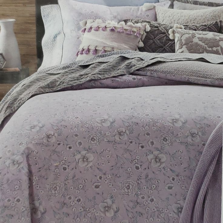 a bed with purple comforter and pillows on top of it, next to a night stand