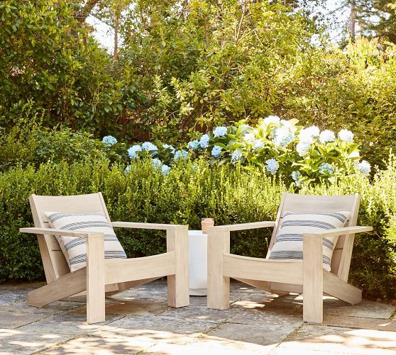 two wooden chairs sitting next to each other on a stone floor in front of bushes