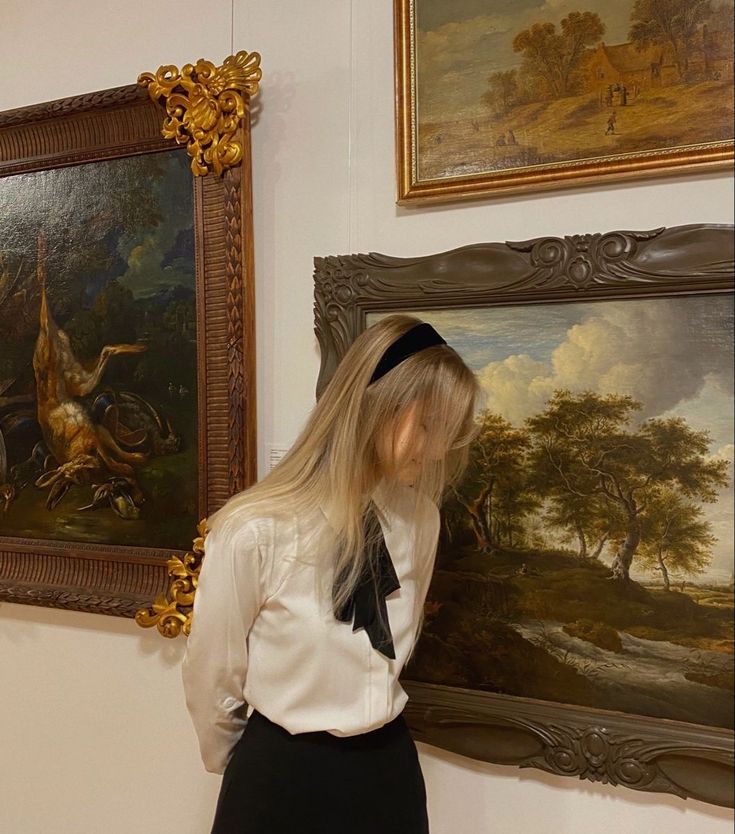 a woman is standing in front of some paintings and posing for the camera with her long blonde hair