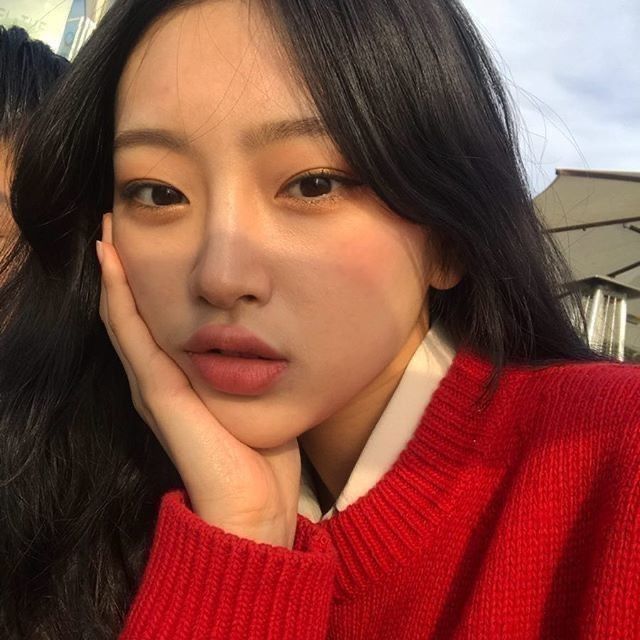 a close up of a person wearing a red sweater with her hand on her chin