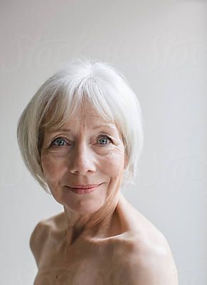 an older woman with white hair and no shirt on posing in front of a window