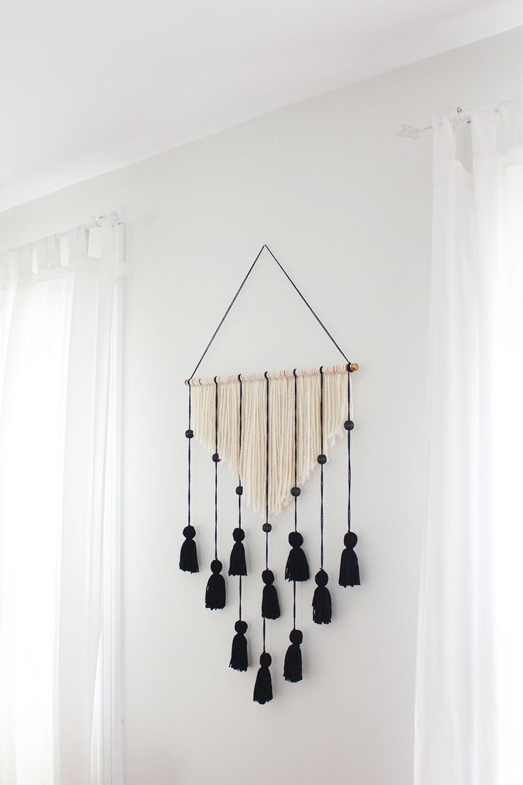 a wall hanging with black tassels on it in a white room next to curtains