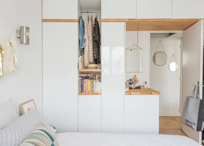 a bed room with a neatly made bed next to a book shelf and cupboards