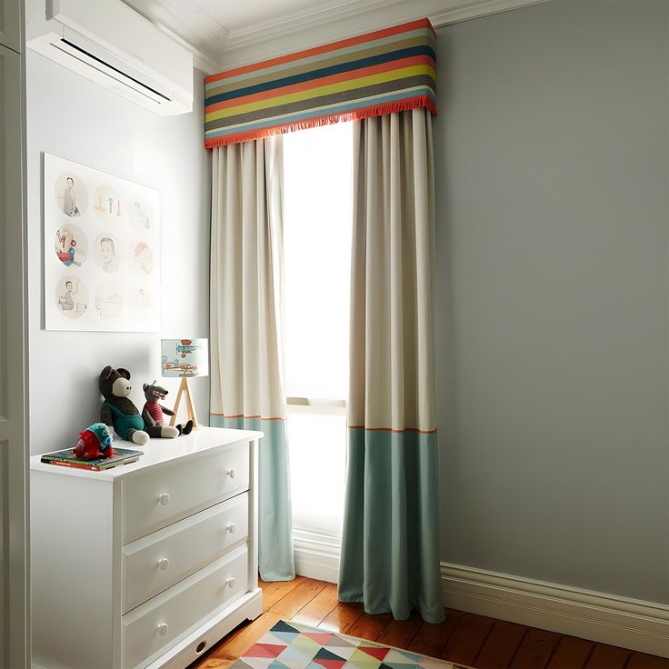 a child's room decorated in white and blue with striped drapes on the window