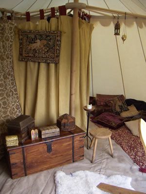 a room with a bed, couch and table in it that has curtains hanging from the ceiling