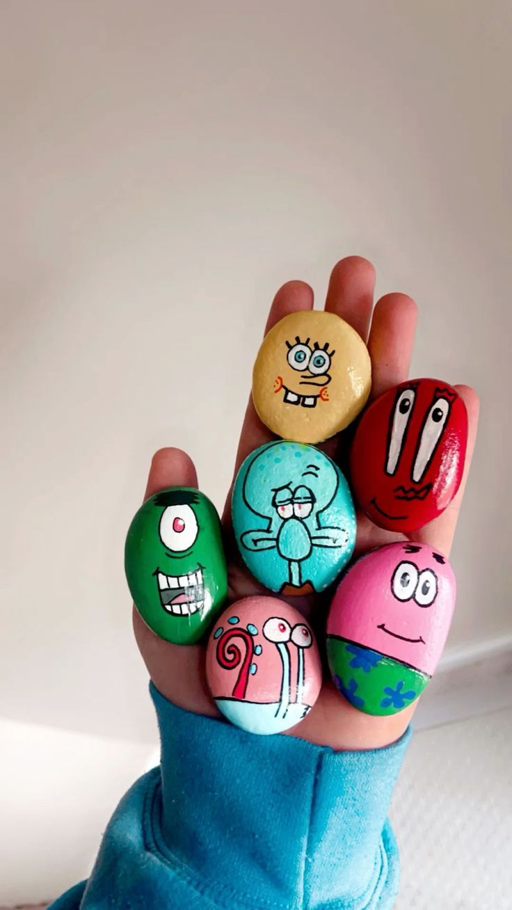 someone is holding up some rocks with cartoon characters painted on them in the palm of their hand