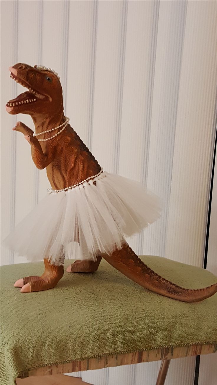 a toy dinosaur in a tutu skirt sitting on top of a chair with its mouth open