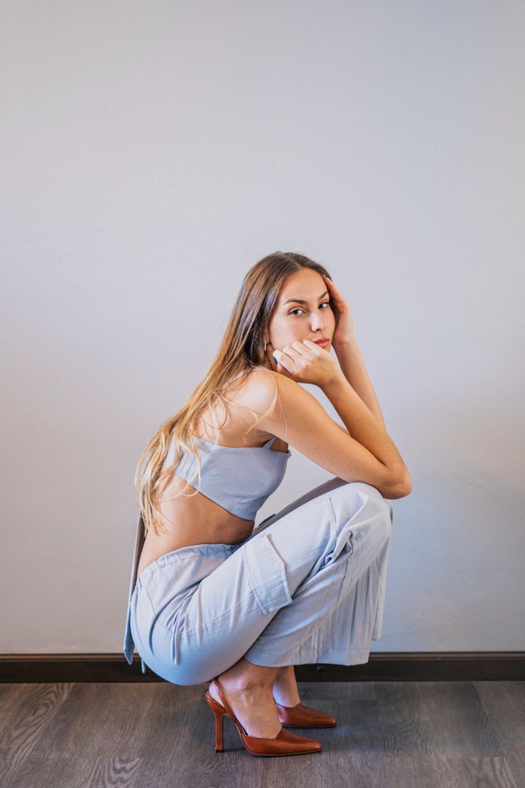 a woman sitting on the floor with her hands behind her head and looking at the camera