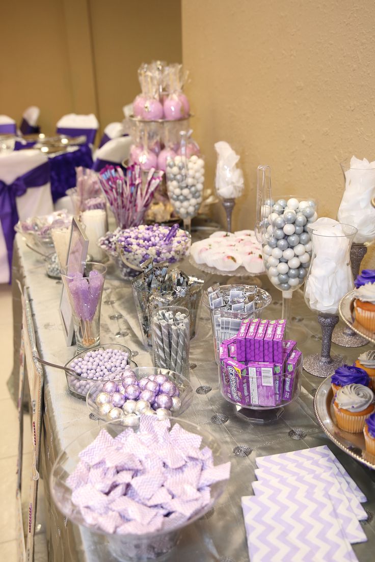 a table topped with lots of cupcakes and candy covered in purple ribboned wrappers