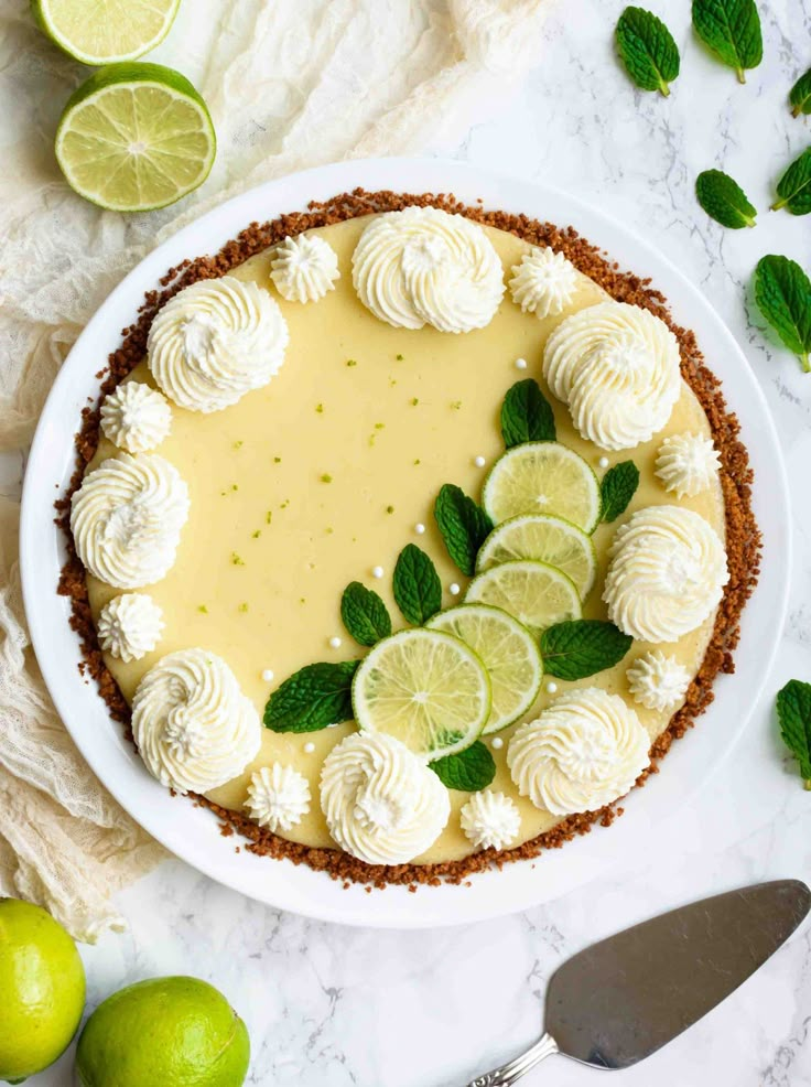 a pie with limes and whipped cream in the middle on a white plate next to sliced limes