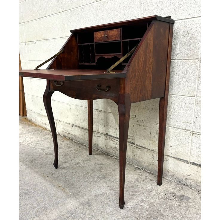 an old wooden desk with a drawer on it's top and bottom shelf, leaning against a white brick wall