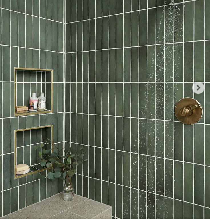 a green tiled bathroom with gold fixtures and shelves on the wall, along with a shower head