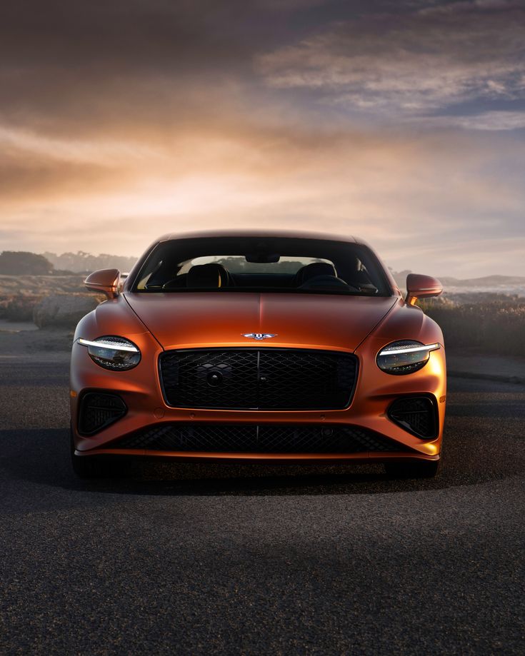 an orange sports car parked on the side of a road at sunset with clouds in the background