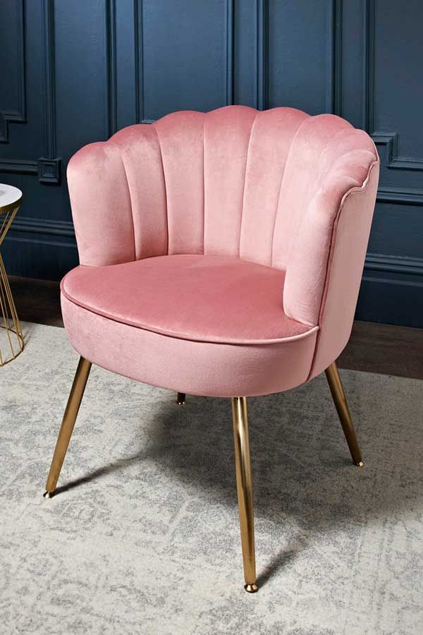 a pink chair sitting on top of a white rug next to a table and blue wall