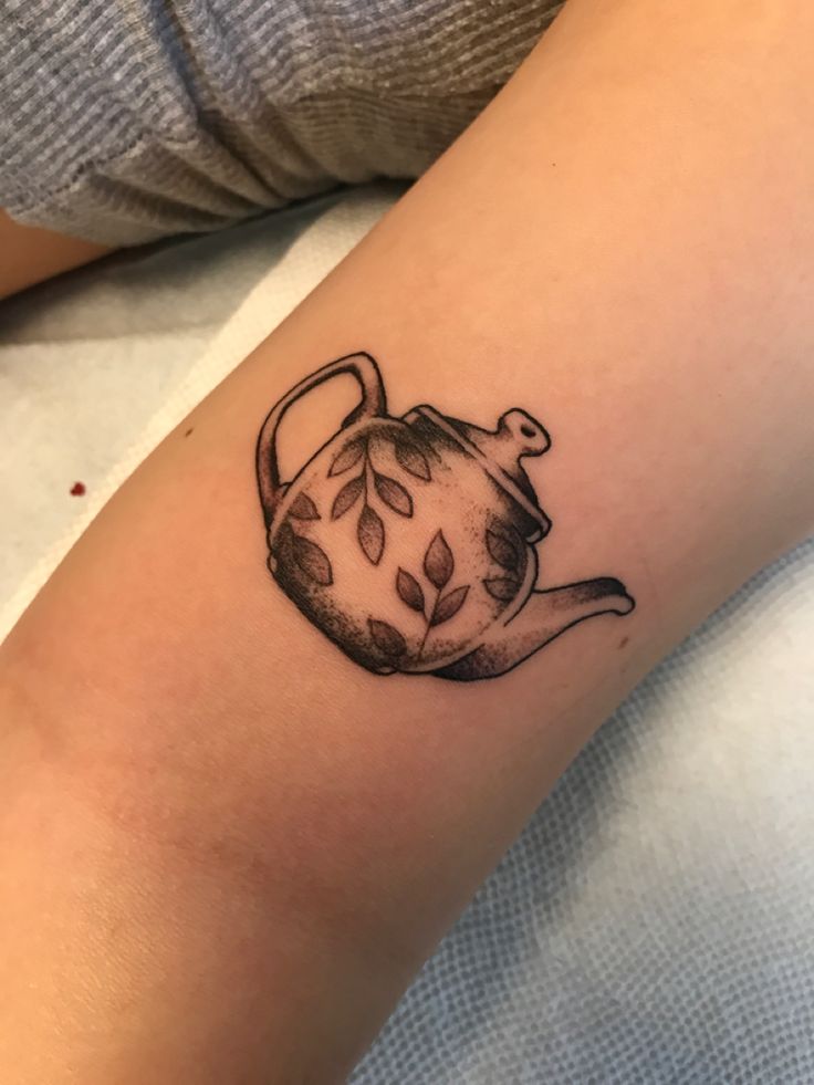 a black and white teapot tattoo on the right arm, with leaves coming out of it