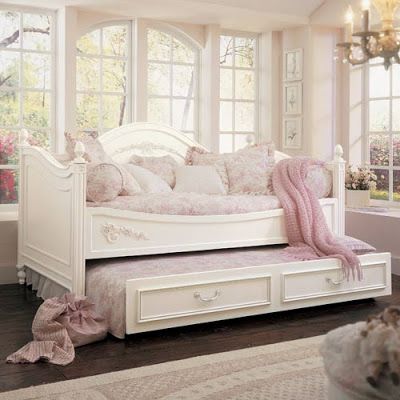 a white daybed with pink pillows and blankets on it in front of two windows