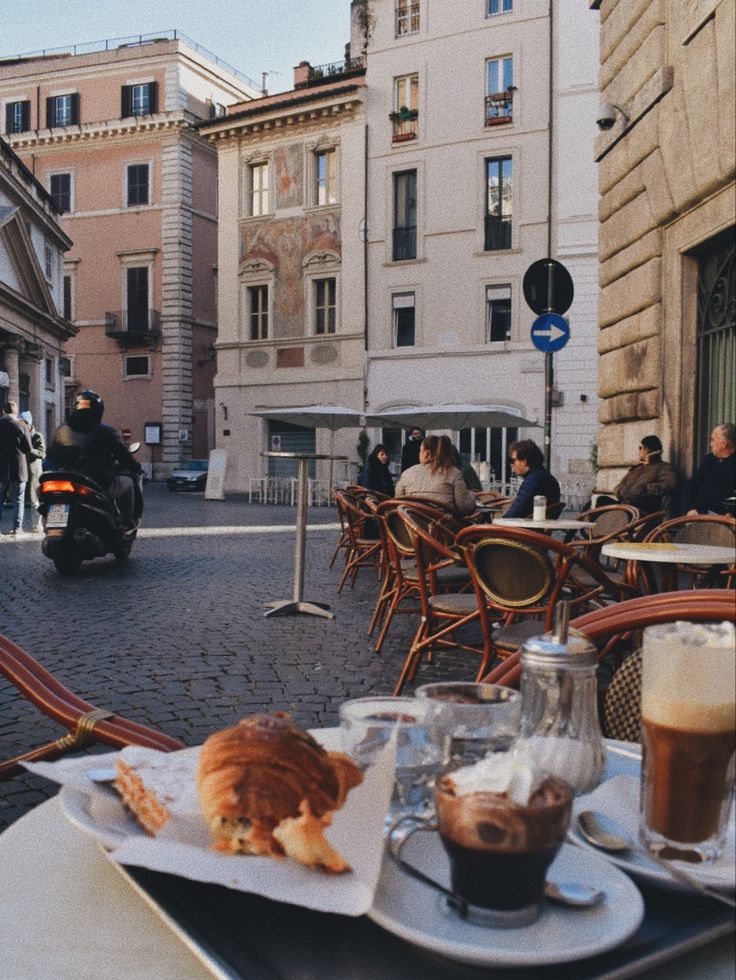 an outdoor cafe with people sitting at tables and eating food on the table in front of them